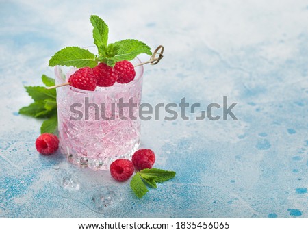 Glass of refreshing summer pink lemonade cocktail with raspberries, ice and mint on blue background. Space for text