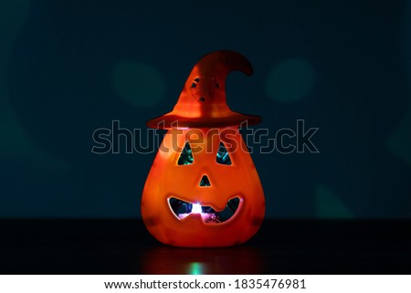 Illuminated Jack O' Lantern pumpkin with witch hat and spooky skull shadow isolated on dark background. Object centered in the frame with empty space for text. Halloween concept