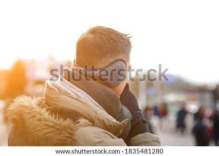 Man wearing ear muffs downtown in cold autumn season. Person with grey earmuffs and gloves while walking in cold winter season. Accessories for the cold season Royalty-Free Stock Photo #1835481280