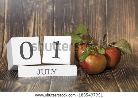 July 1. Day 01 of month. Calendar cube on wooden background with red apples, concept of business and an important event. Summer season.