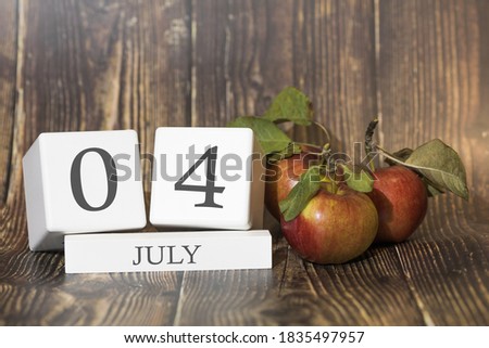 July 4. Day 04 of month. Calendar cube on wooden background with red apples, concept of business and an important event. Summer season.