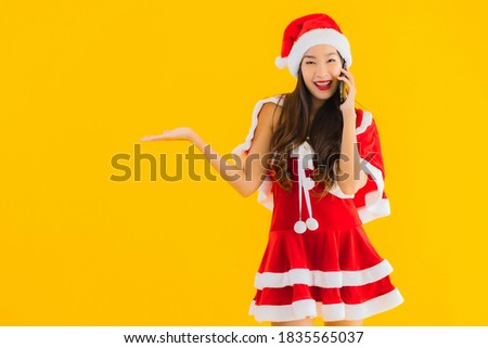 Portrait beautiful young asian woman wear christmas clothes and hat use smart mobile cell phone on yellow isolated background