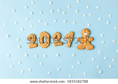 Happy New Year's set of numbers 2021, gingerbread man in face mask from ginger biscuits glazed sugar icing decoration on blue background, minimal seasonal pandemic winter holiday banner