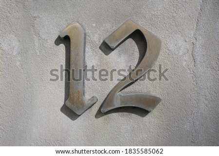 House number 12 on a bright white modern concretye wall.