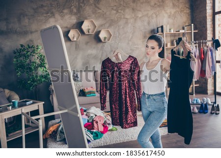 Portrait of her she nice, attractive doubtful girl holding in hand two new chic podium festal dress looking at mirror flattering choosing vs comparing in modern loft industrial interior apartment Royalty-Free Stock Photo #1835617450