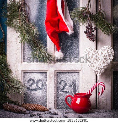 Hand drawn lettering with finger for 2021 Happy New Year on a frozen window decorated with red Santa Claus hat , candy, heart, pine branches with cones. Royalty-Free Stock Photo #1835632981