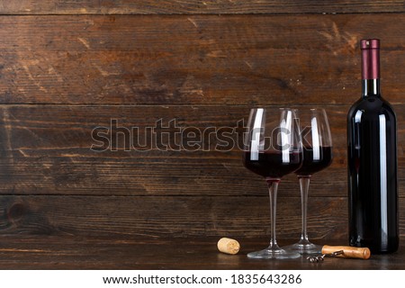 Bottle of wine and two glasses. There is a corkscrew and a cork nearby. Soace for text.