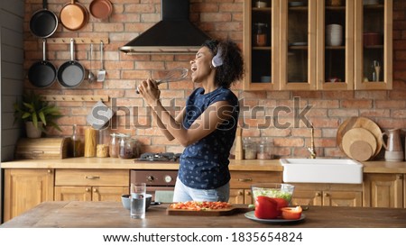 Overjoyed millennial African American woman have fun cooking healthy tasty breakfast in home kitchen. Happy playful young biracial girl sing entertain enjoy good morning prepare food at countertop. Royalty-Free Stock Photo #1835654824