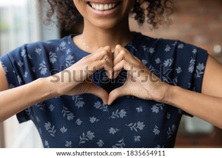 Crop close up of happy African American woman feel grateful thankful show heart sign spread love and care. Smiling biracial female volunteer make hand gesture support ill sick people patients. Royalty-Free Stock Photo #1835654911