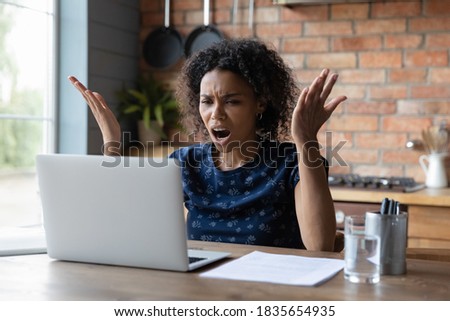 Angry young African American woman look at laptop screen distressed with slow internet connection. Mad biracial female frustrated by computer problem or spam working on gadget at home office. Royalty-Free Stock Photo #1835654935