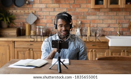Young African American male vlogger influencer in headphones record video blog on smartphone at home. Millennial biracial man blogger talk speak shoot live broadcast on cellphone for social media. Royalty-Free Stock Photo #1835655001