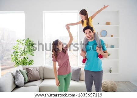 Photo of positive cheerful three people mom dad play weekend game, carry shoulders small kid girl hold hand in house indoors