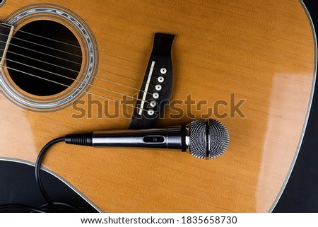 The neck of a classic six-string guitar and a silver microphone on a black background. guitar and accessories. creativity and playing the guitar