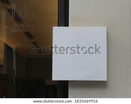 Modern blank generic sign outside a restaurant or retail store. White square block plaque for store logo. The store is in the background