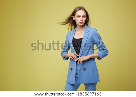Fashion photo of a beautiful elegant young woman in a pretty blue suit, jacket, pants, trousers posing over yellow lemon background. Studio shot, portrait. Yellow and blue colors