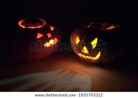 two Halloween pumpkins, turned to each other frightening faces, glowing in the dark with red and yellow mesmerizing light