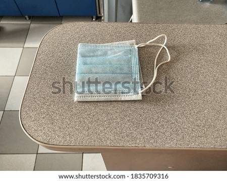 Disposable blue medical face shield rolled in half, lying on a gray surface during the day.