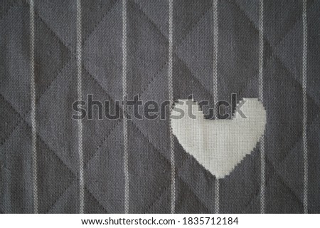 Grey quilted fabric background with white stripes and a heart in the lower right corner