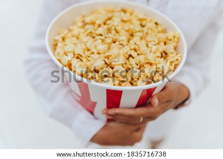 Close-up photo of a young sweet girl, who is holding a tube of popcorn in her hands.