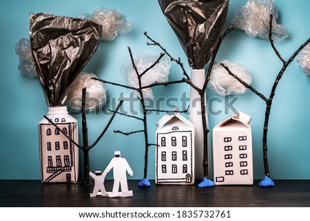 A conceptual illustration showing the polluted smoke from a factory chimney over a city and a family. A city made of milk cartons and garbage bags. Do it yourself.