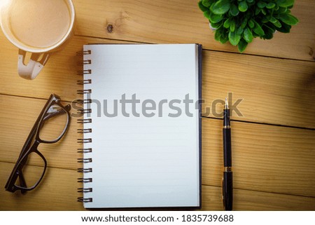 Blank notebook with pen and with glasses next to cup of coffee on wooden table,business concept.