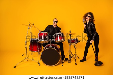 Full size photo of famous rock group guy plays instruments beat drum, sticks attractive girl sings mic night club performance show concert wear black leather outfit isolated yellow background
