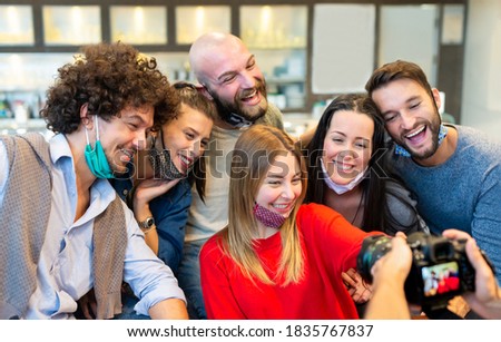 smiling group of caucasian people wearing protective face mask posing for a picture together in front of a photographer reflex camera. mates taking a pic together. concept about new normal lifestyle