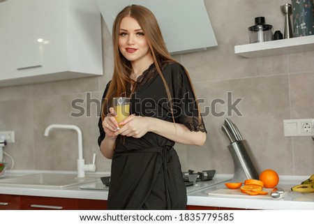 Woman in a kitchen. Lady in a black pajamas. Famale with orange juice.