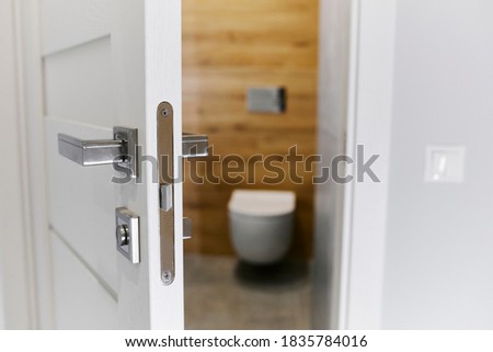 Half opened door into the cozy home interior. Interior of light modern restroom. Chrome door handle close up