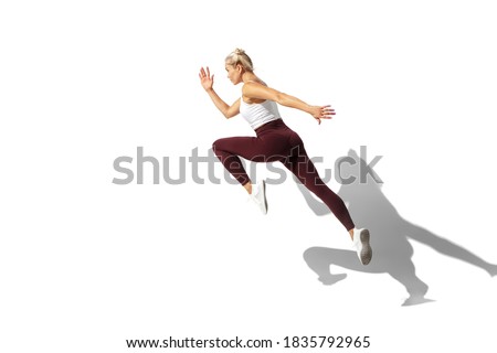 Running. Beautiful young female athlete practicing on white studio background, portrait with shadow. Sportive fit model in motion and action. Body building, healthy lifestyle, style concept.