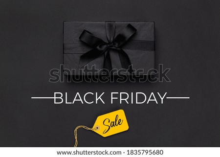 Black gift box and tied with black bow and yellow price tag on black background. Black friday concept, top view.