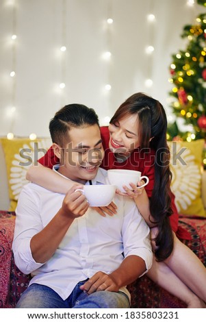 Happy beautiful young Vietnamese couple drinking delicious hot chocolate at home