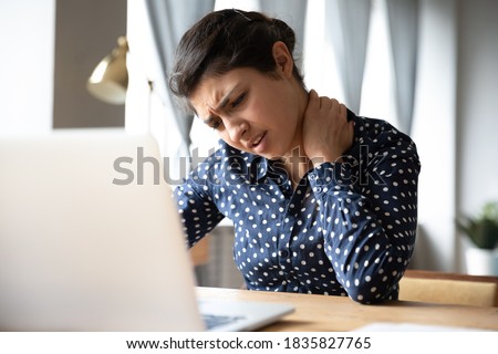 Pinched nerves, tensed sore muscles, fibromyalgia ache due sedentary lifestyle and incorrect posture concept. Indian ethnicity frowning woman sitting at desk in front of laptop, touch neck feels pain Royalty-Free Stock Photo #1835827765