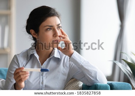 Indian ethnicity woman holding pregnancy test looking out the window deep in sad thoughts about health problems and infertility feels troubled by result, bad news, unwanted pregnancy, abortion concept Royalty-Free Stock Photo #1835827858