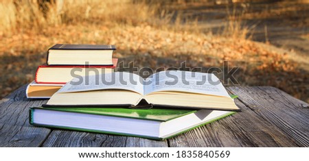 Open book in a stack of books on a table in an autumn park.