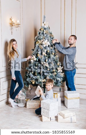 happy young family with one child holding christmas gift and smiling at camera. happy family mother father and baby at christmas tree at home