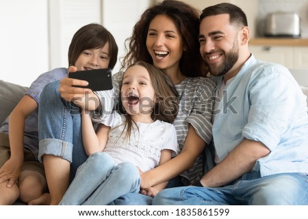 Overjoyed parents and two adorable kids posing for selfie together, cute smiling girl holding smartphone, photographing, happy mother and father with children having fun with gadget at home