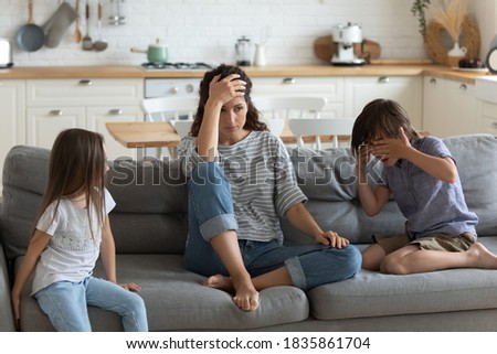 Tired exhausted mother having problem with naughty noisy kids, sitting on couch, touching forehead, suffering from headache, difficult child, children tantrum and manipulation concept Royalty-Free Stock Photo #1835861704