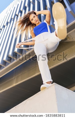 View from below of young girl throwing her foot in the air in urban background.