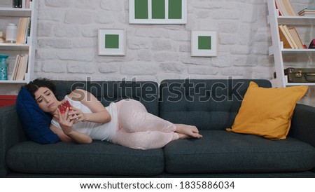 A woman lying on the sofa is taking a selfie with her phone. The concept of working and spending time at home.