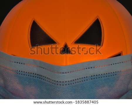 Close up view of Halloween pumpkin lantern wearing a medical facial mask as a symbol of disease control and virus infection and coronavirus or covid-19 with black background. Selective focus