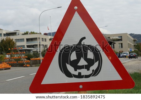 A triangle road sign with a carved pumpkin at the road side. 
In the background a farm shop displaying products of a local  pumpkin farm. Ideal for Halloween and Thanksgiving.
