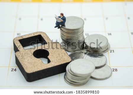 Money , Planning and Security Concept. Businessman miniature figure people sitting and reading a newspaper on stack of coins with wooden key lock symbol on calendar.