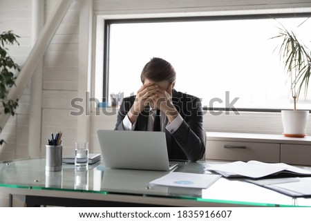 Unhappy young male manager covering head with hands, suffering from pressure at work or feeling unwell due to overload. Overworked stressed businessman workaholic having headache, needs rest. Royalty-Free Stock Photo #1835916607