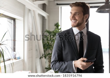 Head shot happy young dreamy ceo manager in formal wear holding mobile phone in hands, thinking of business opportunity alone in office, smiling leader planning workday, feeling excited of good news. Royalty-Free Stock Photo #1835916796