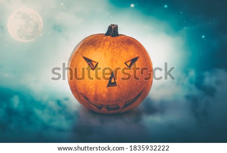 Pumpkin with Angry Carved Face over Cloudy Nighttime Background. Spooky Night with Full Moon. Halloween Celebration. Traditional American Holiday.