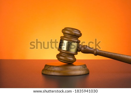 Wooden gavel on wooden surface against orange background, close up Royalty-Free Stock Photo #1835941030