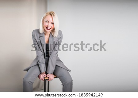 young woman with blond hair sits on a chair and leans on the chair with her hands. girl in gray suit