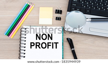 NON PROFIT inscription on an open notebook on the desktop next to it lies a laptop, a pen, pencils, a magnifying glass. CAPITAL LETTERS BUSINESS CONCEPT