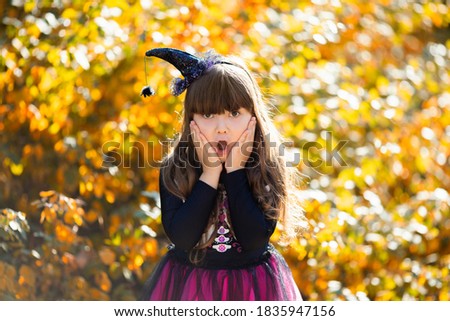 Adorable little witch girl ready for halloween and trick or treat, autumn yellow trees at the background